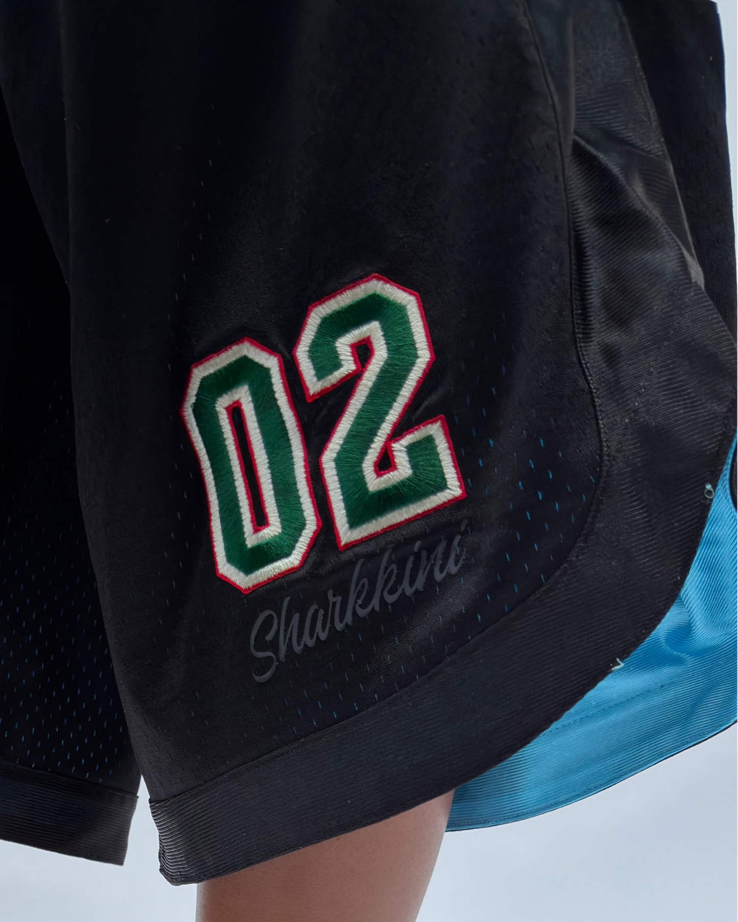 A person wearing black wedge flip-flop sandals with white and green 'bebe' branding, paired with black athletic shorts featuring a green and white '02' graphic.